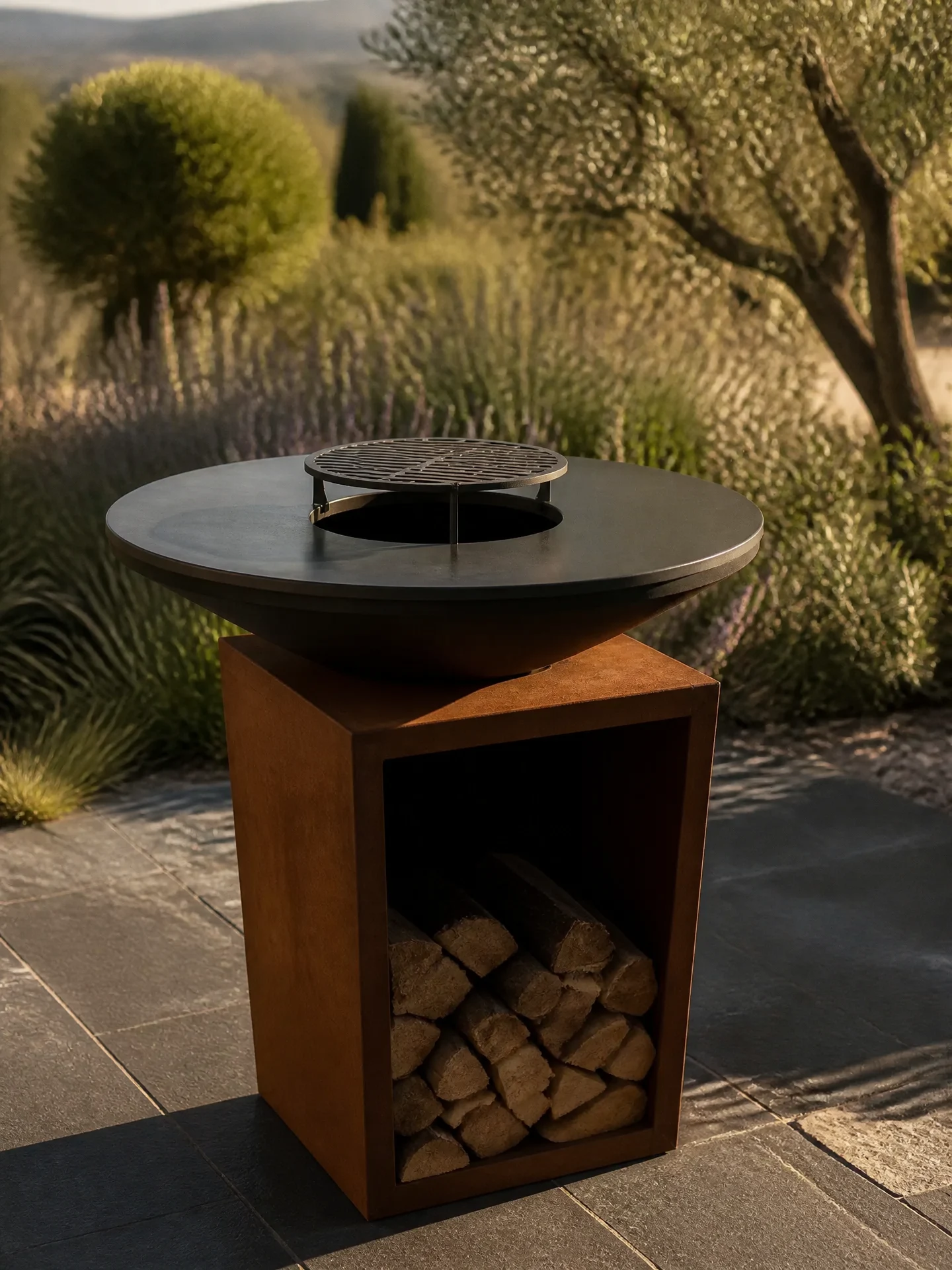 Brasero artisanal en acier corten avec range-bûches intégré sur terrasse en pierre